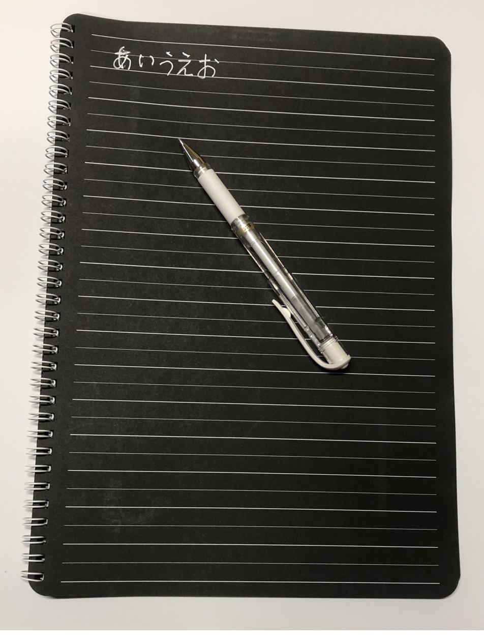 ブラックノートに白ペンで「あいうえお」と書いている写真